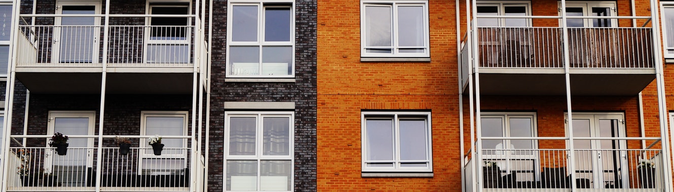 Exterior of orange and black brick apartment building with windows and balcony.